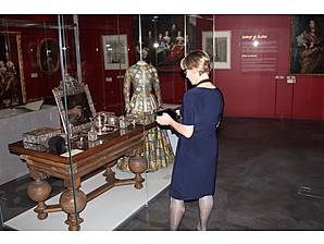 Besucherin des Maritimen Museum erkundet mit dem Dorengo Handheld das Exponat - ein opulenter Holztisch mit silbernen Gegenständen wie Bilderrahmen, Dosen, Tablett