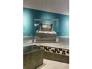 Gemälde, das eine Kriegsflotte abbildet. Im Vordergrund eine mit Sand gefüllte Kiste voller Kanonenkugeln